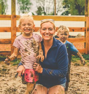 Three people playing and getting muddy together in an outdoor enclosure on a sunny day.