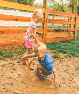 Children playing and splashing in a muddy outdoor area with orange wooden fence.