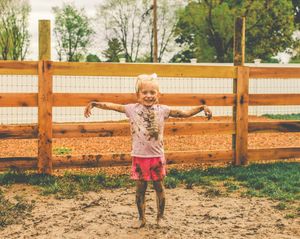 Children playing in a fenced dirt area on a sunny day.