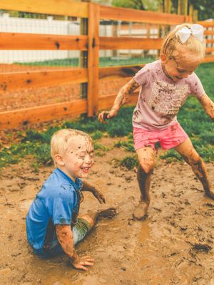Children play and splash in a muddy puddle on a sunny day, creating joyful outdoor memories.
