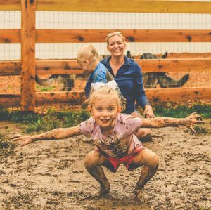Children play and splash in a muddy outdoor area with wooden fencing in the background.
