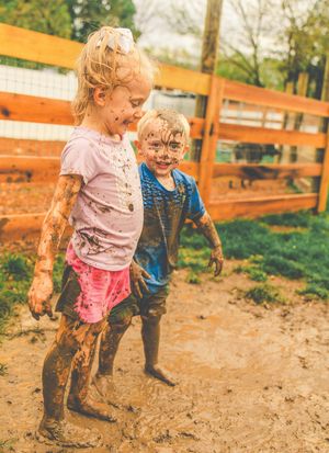 Children playing and splashing in a muddy outdoor area with wooden fencing.