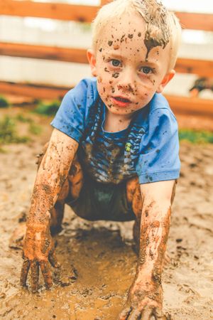 A young child covered in mud plays in a dirt pit while wearing a blue t-shirt.