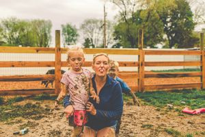 Kids having fun and getting messy in a fenced muddy play area.