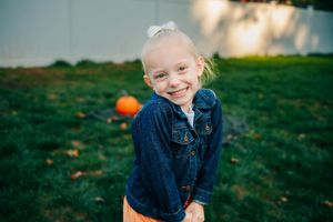 A child in a denim jacket plays outdoors with a bright orange ball on a grassy field in autumn.