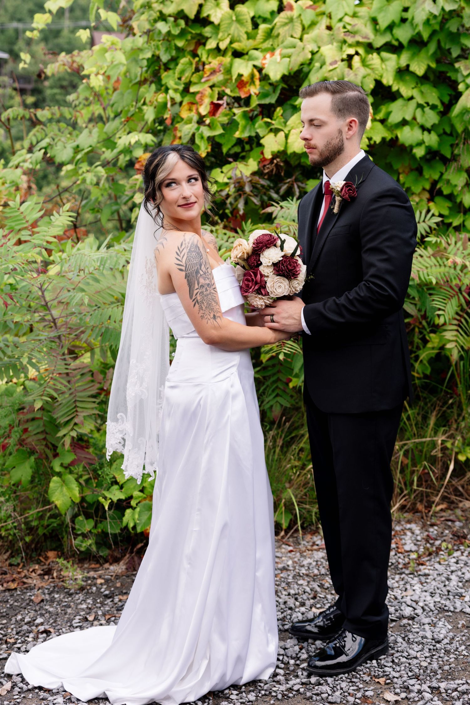 A couple in wedding attire share an intimate moment together outdoors against a backdrop of lush green foliage.