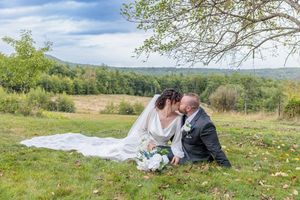 Bride and groom share a kiss while seated on grassy hillside with scenic countryside view behind them. The Venue at Ponderosa Milton NH