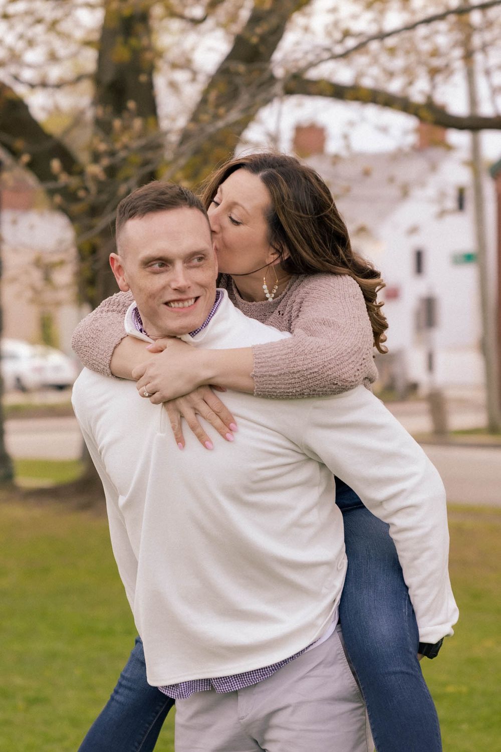 A woman kisses a smiling man on the cheek while he gives her a piggyback ride in a park.