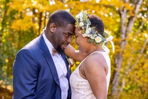 Black couple in wedding attire share tender forehead touch surrounded by vibrant autumn foliage
