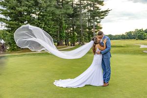 Groom dips bride in mermaid gown as her veil flows dramatically on lush golf course green. Stonebridge Country Club Goffstown NH.