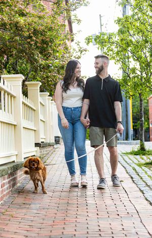 A happy couple walks their golden-brown Cavalier King Charles Spaniel on a charming brick sidewalk in Historic Portsmouth New Hampshire.