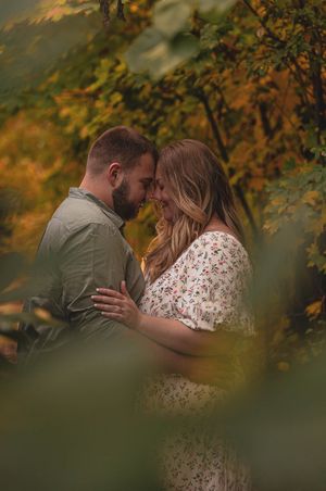 Couple touching foreheads romantically surrounded by colorful autumn foliage.