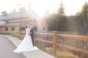 Bride and groom sharing a romantic moment at sunset near a rustic wooden fence. Barn at Bull Meadow Concord NH