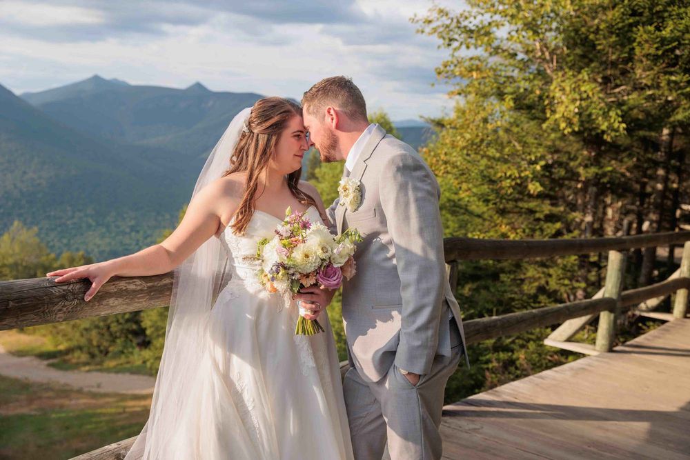 Bride and groom share a romantic moment on a White mountain overlook deck, In North Conway NH with scenic peaks in the background.