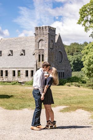 A couple shares a kiss in front of a historic stone church on a sunny summer day.