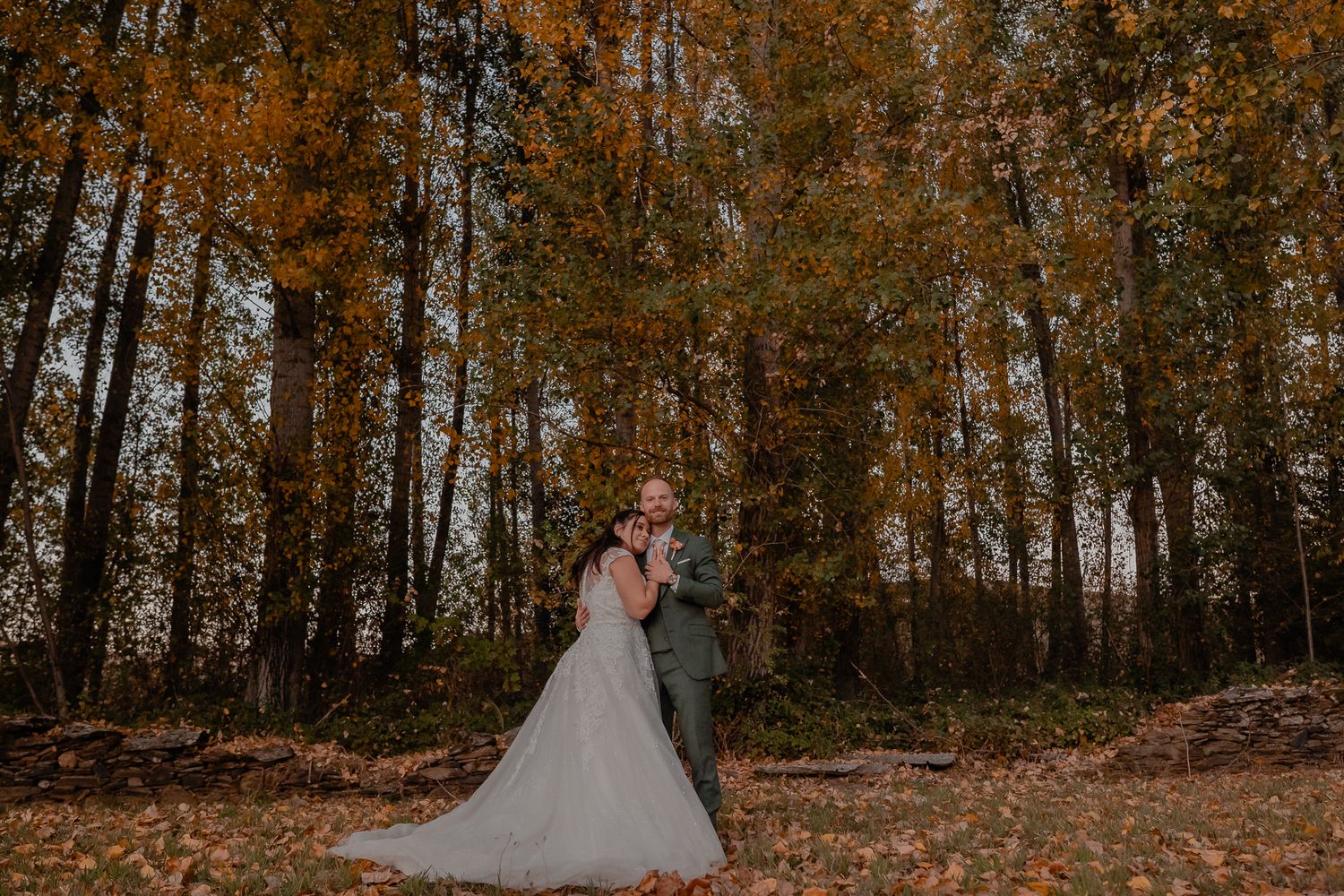 Wedding couple sharing an intimate moment in a forest with golden autumn leaves.
