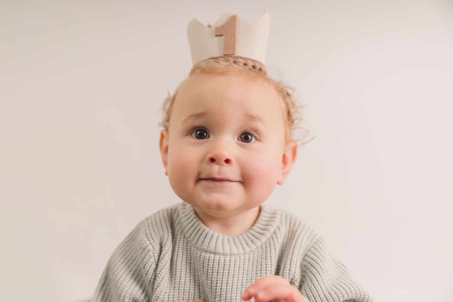 Baby in gray sweater smiles sweetly during studio portrait session. Photographer. Hull. East Yorkshire.
