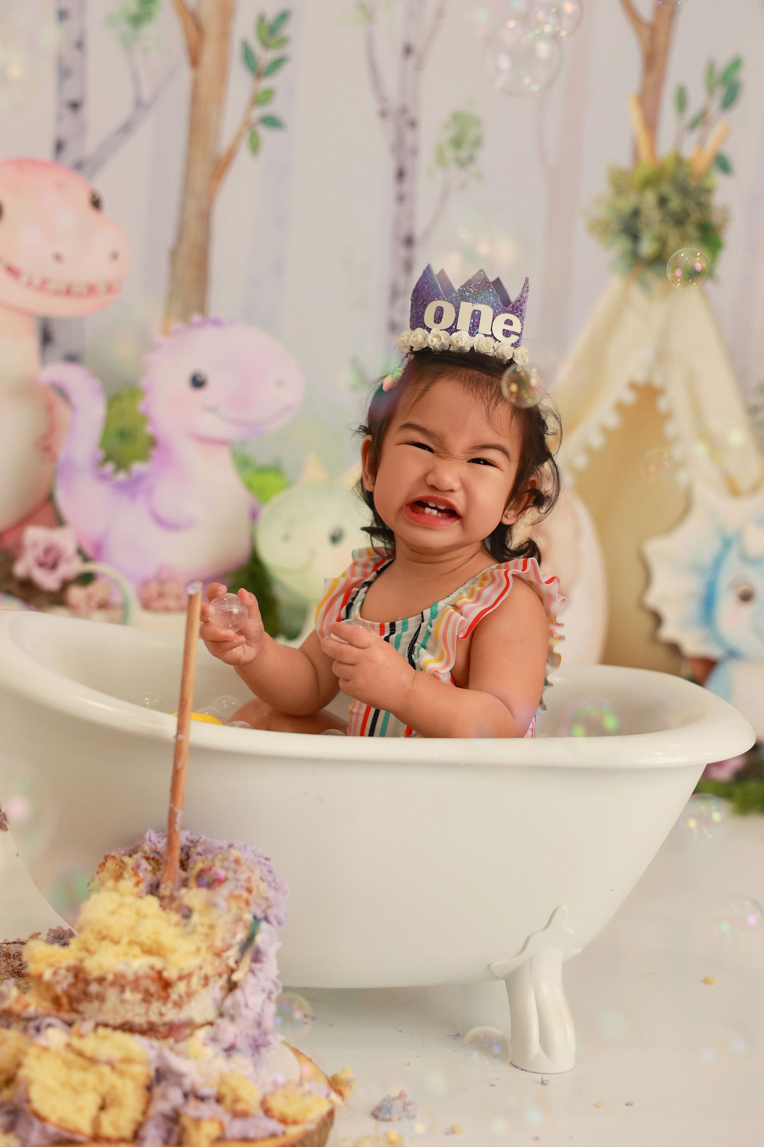 A whimsical first birthday celebration with a purple cake and bath setup against a woodland-themed backdrop.