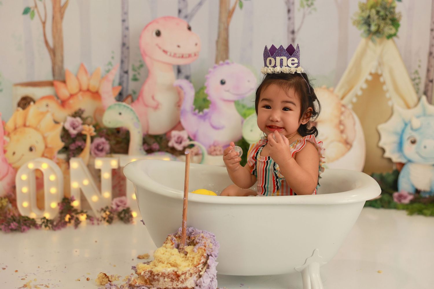 A child in a pink dress smiles and plays on a white floor with stuffed animals and fairy lights creating a magical scene.
