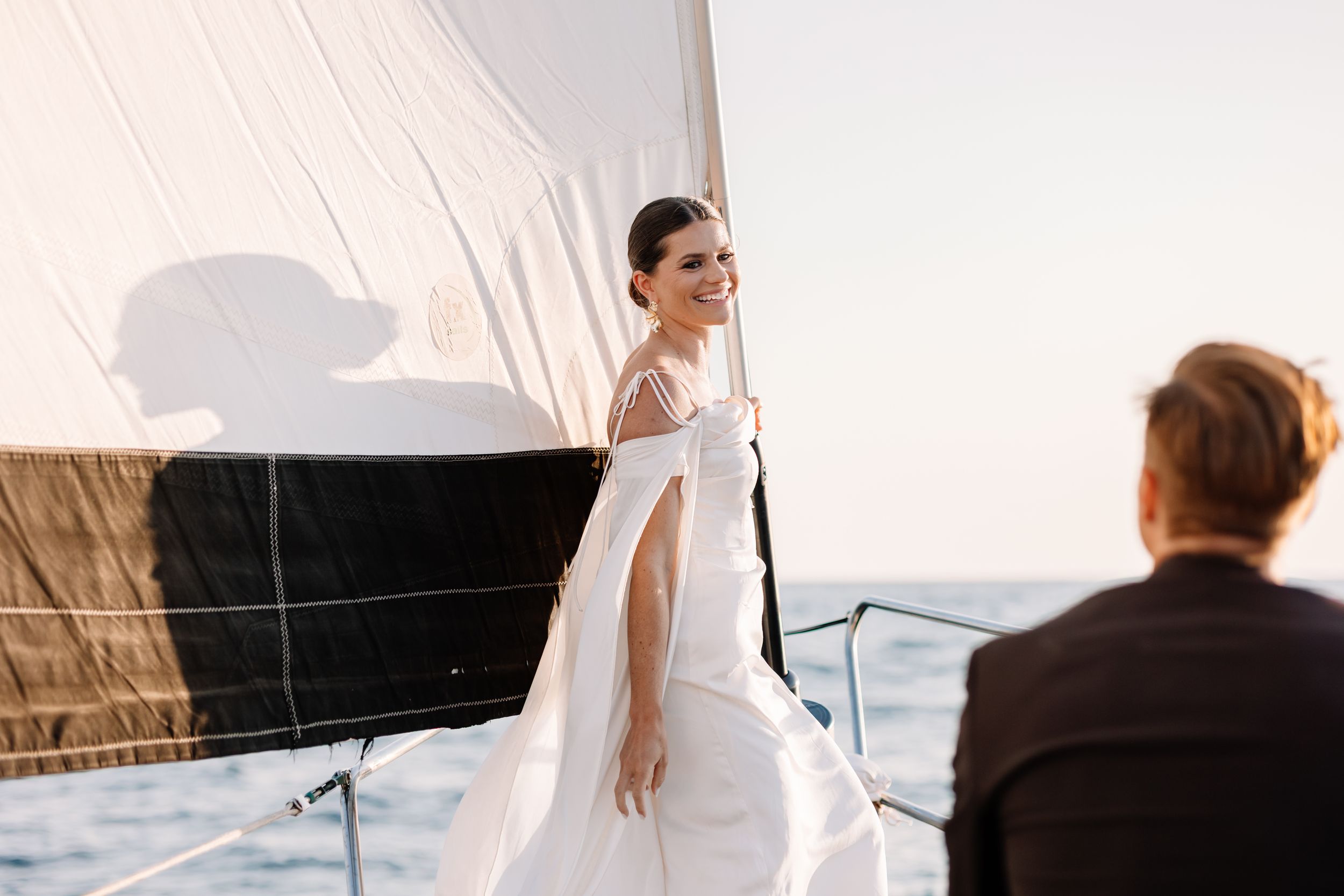 Elegant couple in wedding attire posing on a yacht during sunset.