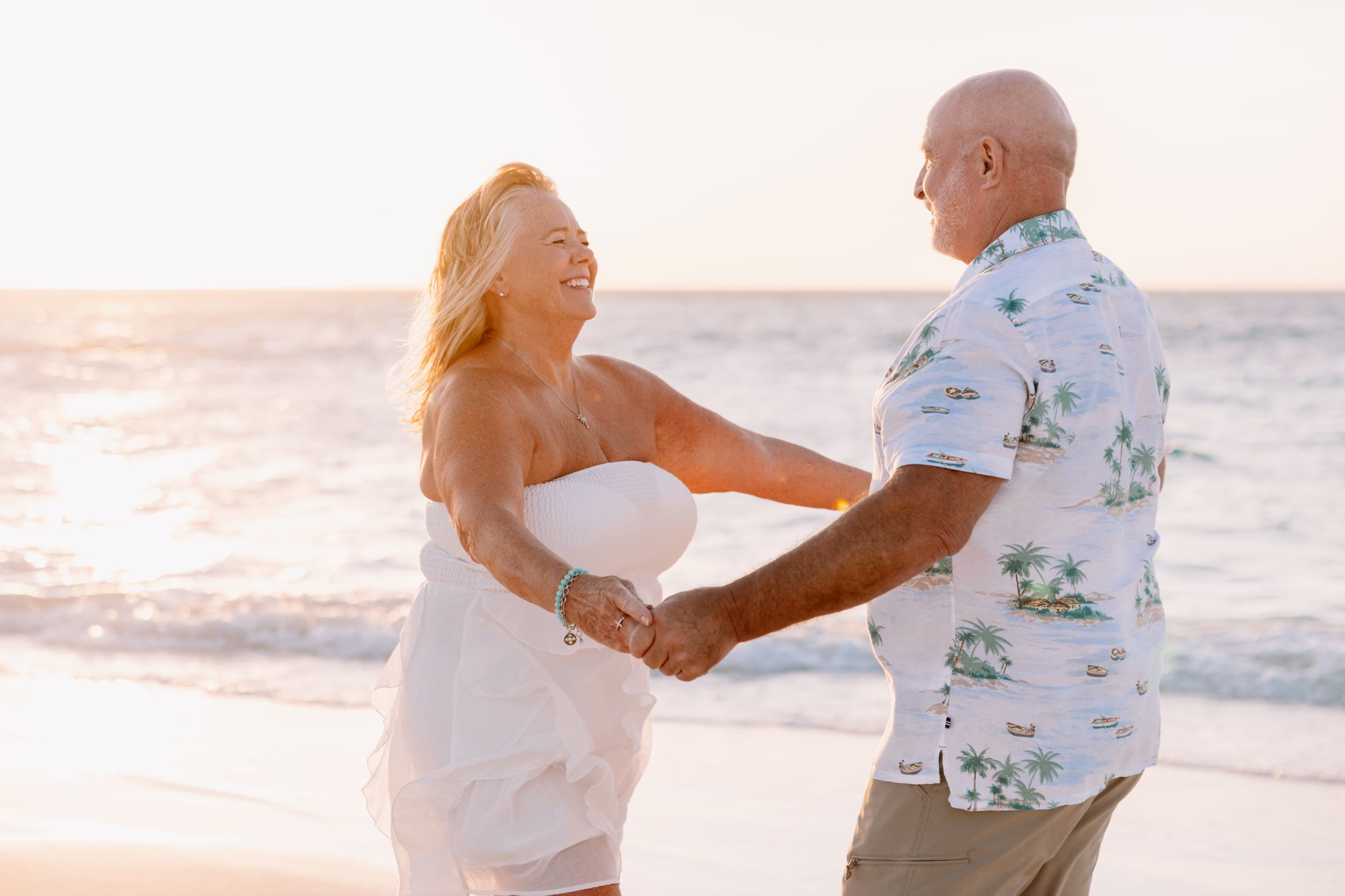 Couple dancing together on a sunny beach at sunset with ocean waves in the background.