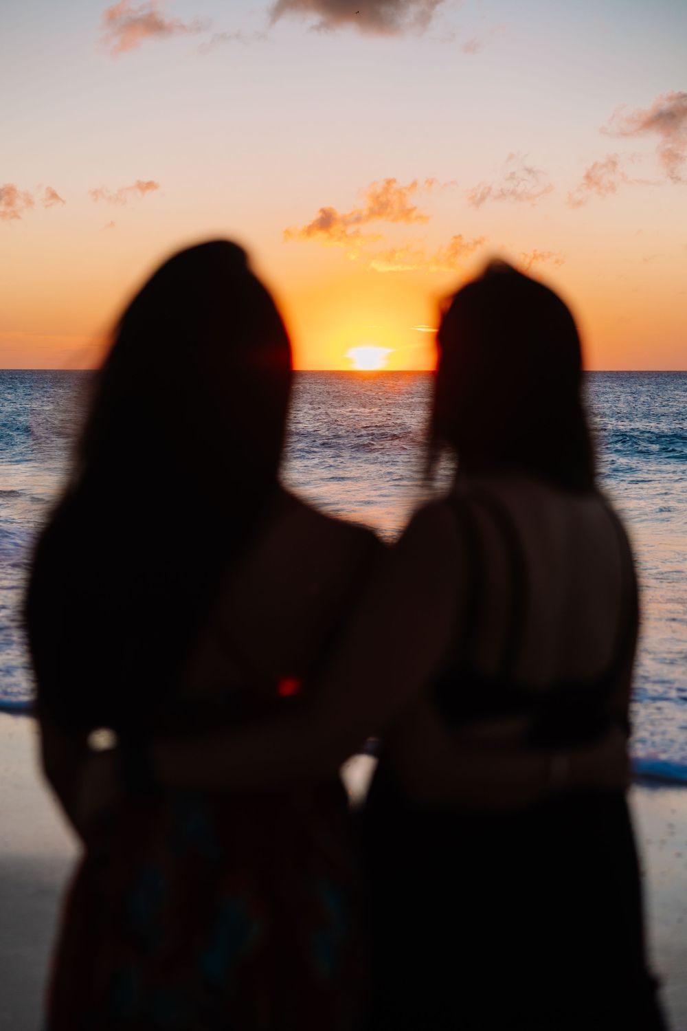 Silhouettes of two people watching a vibrant orange sunset over the ocean from a beach.