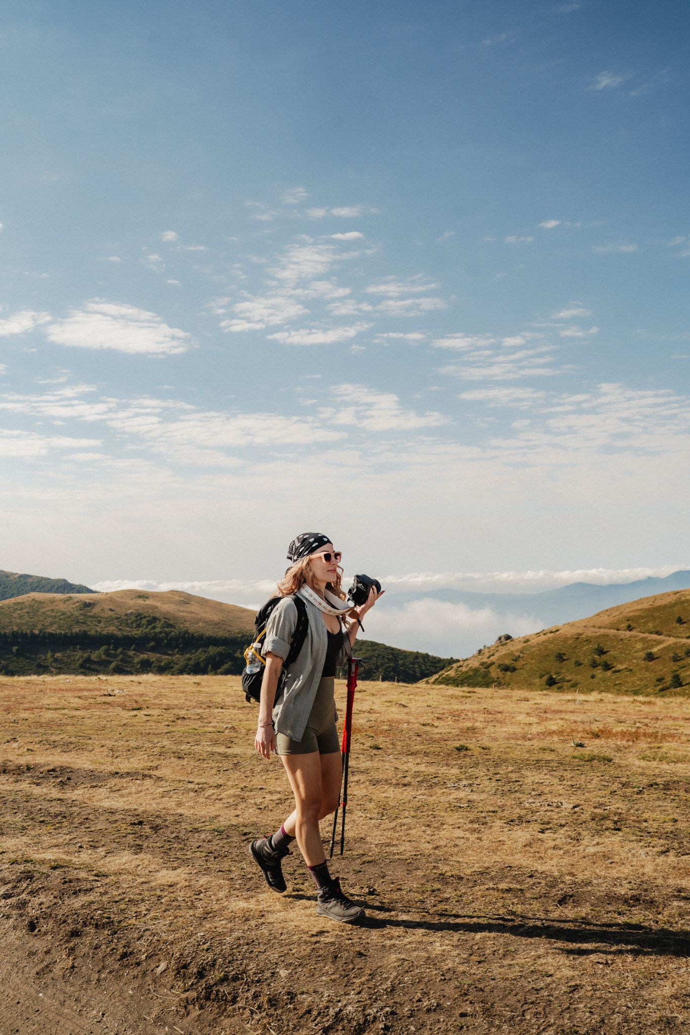 Hikers traverse a scenic mountain trail under blue skies and scattered clouds on a sunny day.