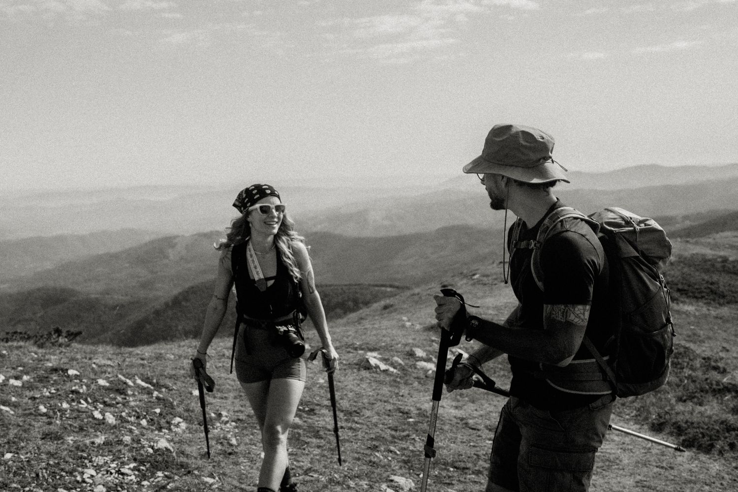 Black and white photo of hikers with trekking poles exploring a mountainous terrain on a sunny day.
