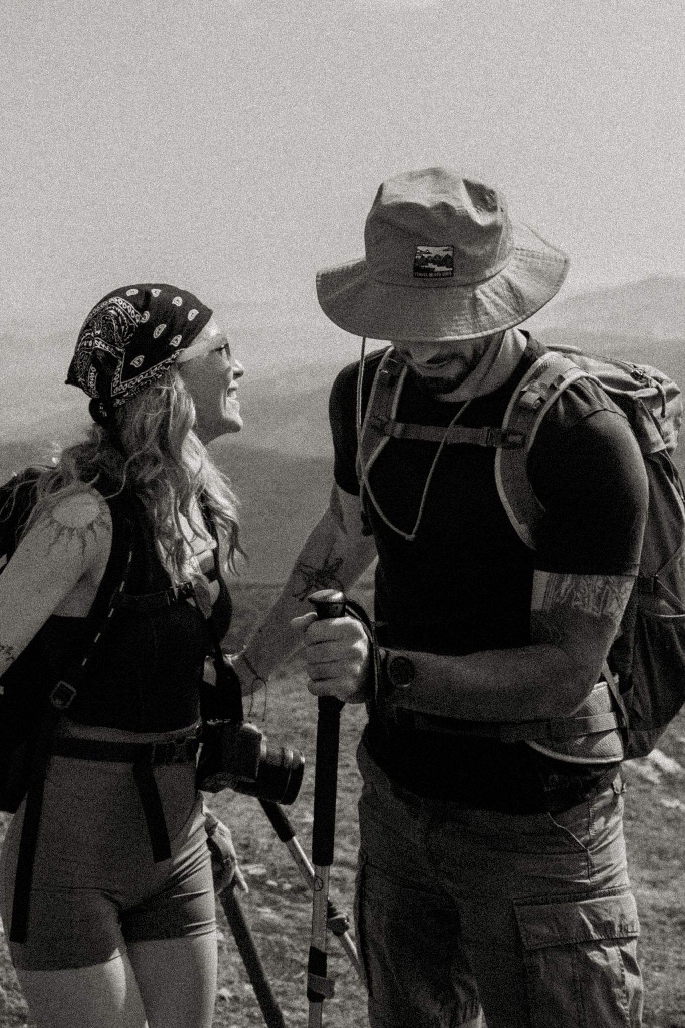 Two hikers share a moment on a mountain trail in black and white photography.