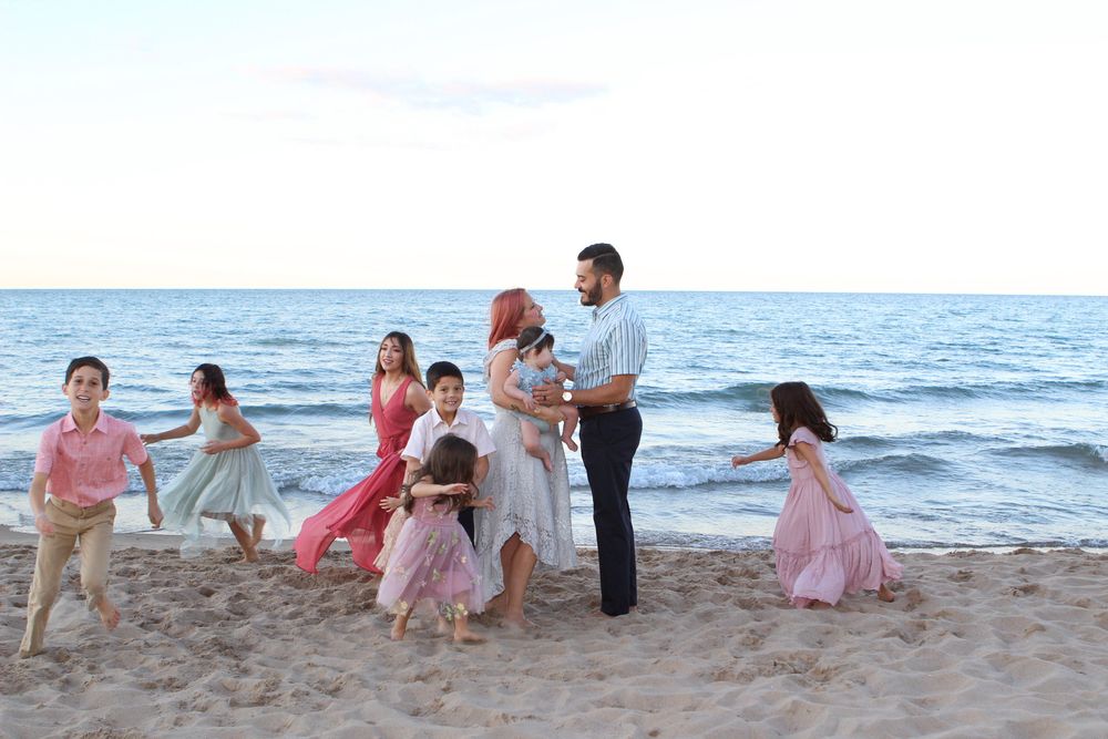 Extended family playing and walking together along beach shoreline at sunset.