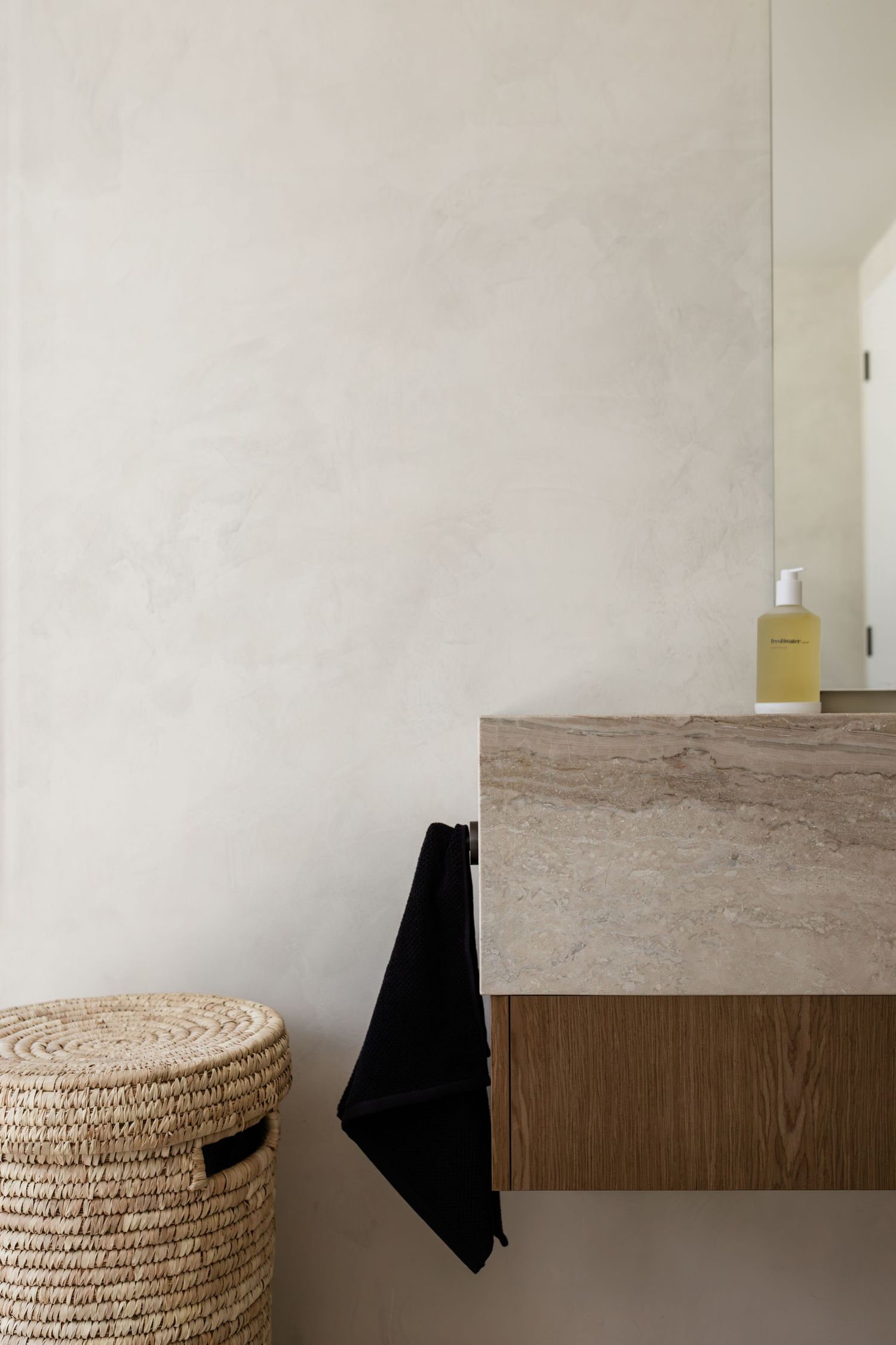 Minimalist bathroom interior with white walls, wooden shelf, and woven basket storage against neutral tones.