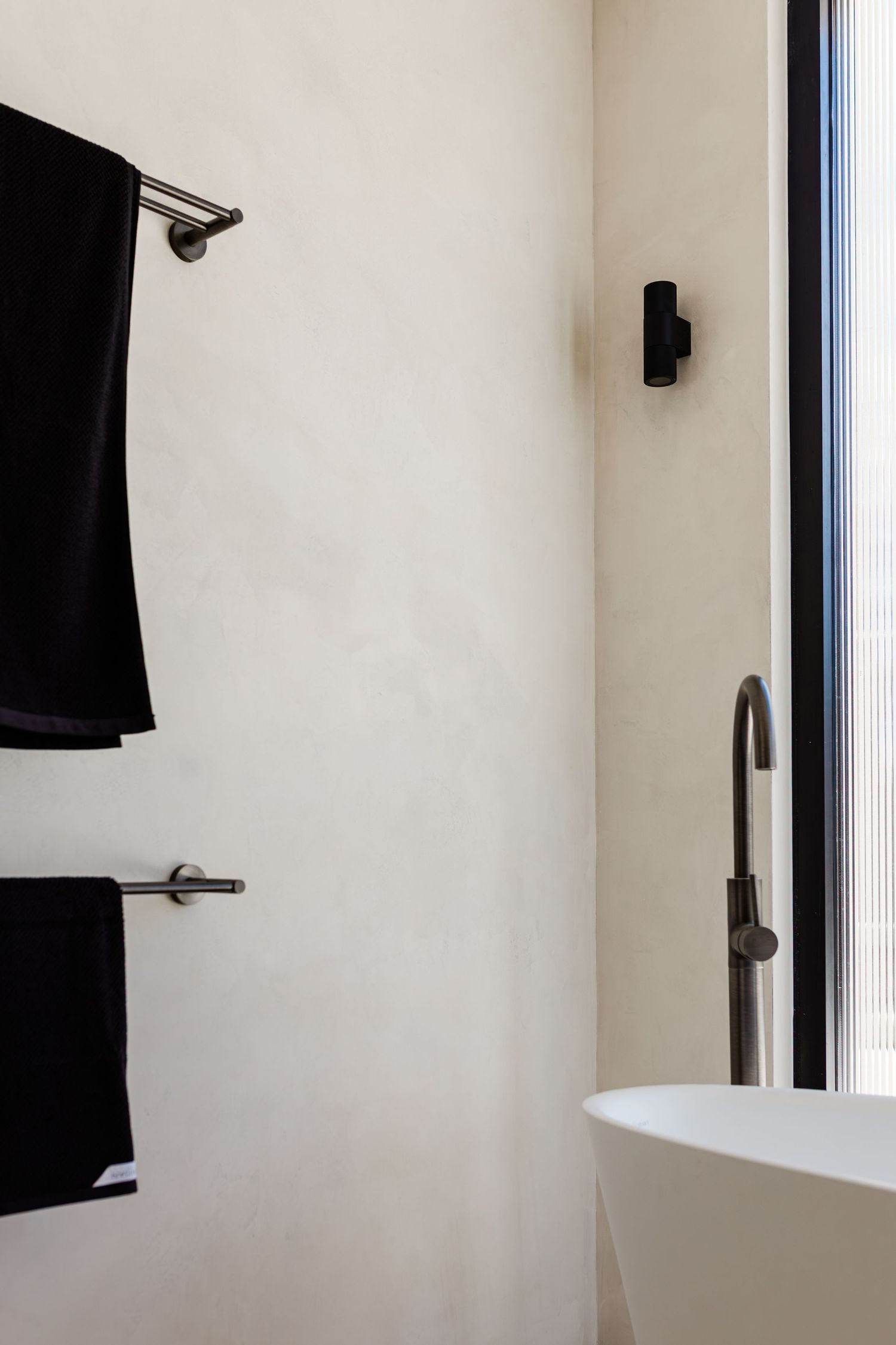 Minimalist white bathroom wall with black towels and modern fixtures in a clean, contemporary design.