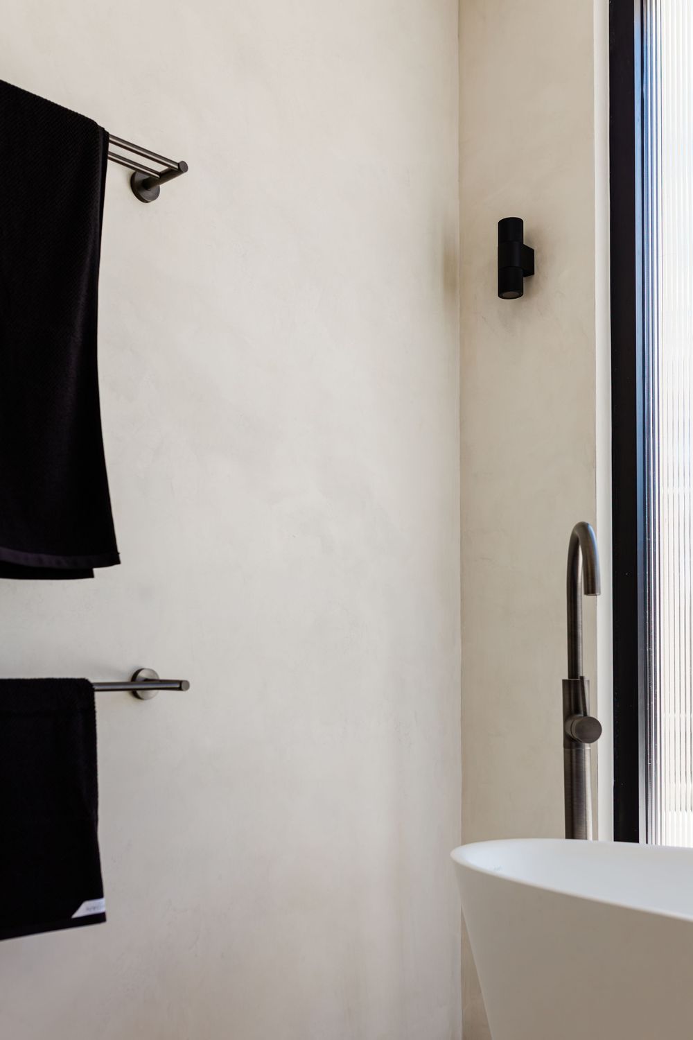 Minimalist white bathroom wall with black towels and modern fixtures in a clean, contemporary design.