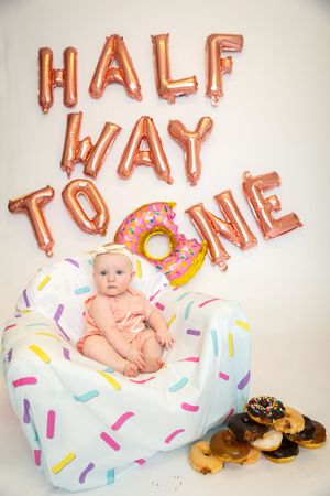 A baby photo series with rose gold balloon letters and a donut-themed setup featuring colorful sprinkle decorations.