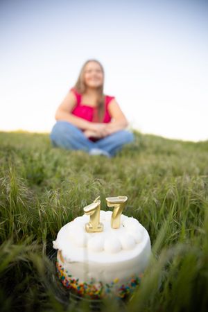 Birthday cake with number 17 candles sits in green grass during an outdoor celebration photoshoot.