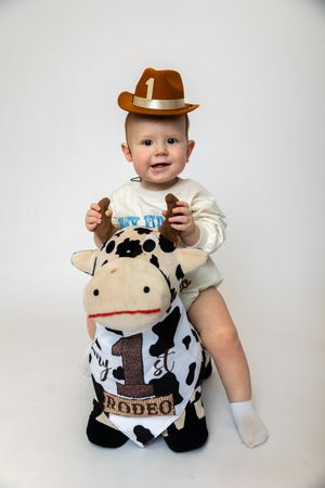 A series of three photos showing a baby wearing a western-themed cowboy outfit with cow print patterns against a white background.