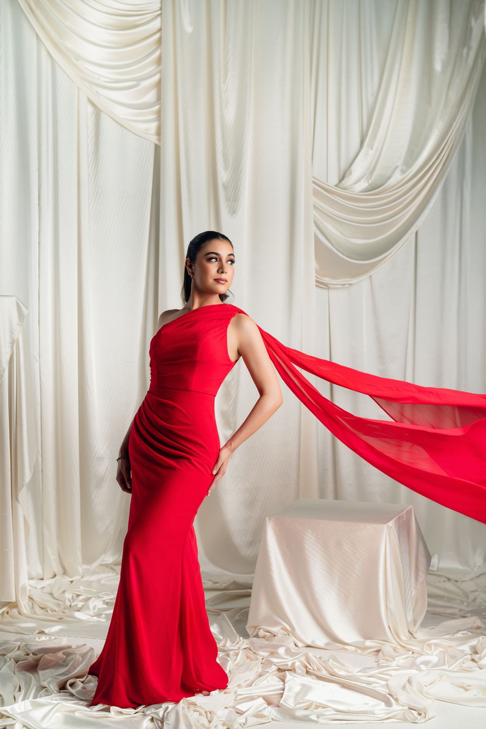 Dynamic fashion poses in a red flowing dress against white draped studio backdrop.