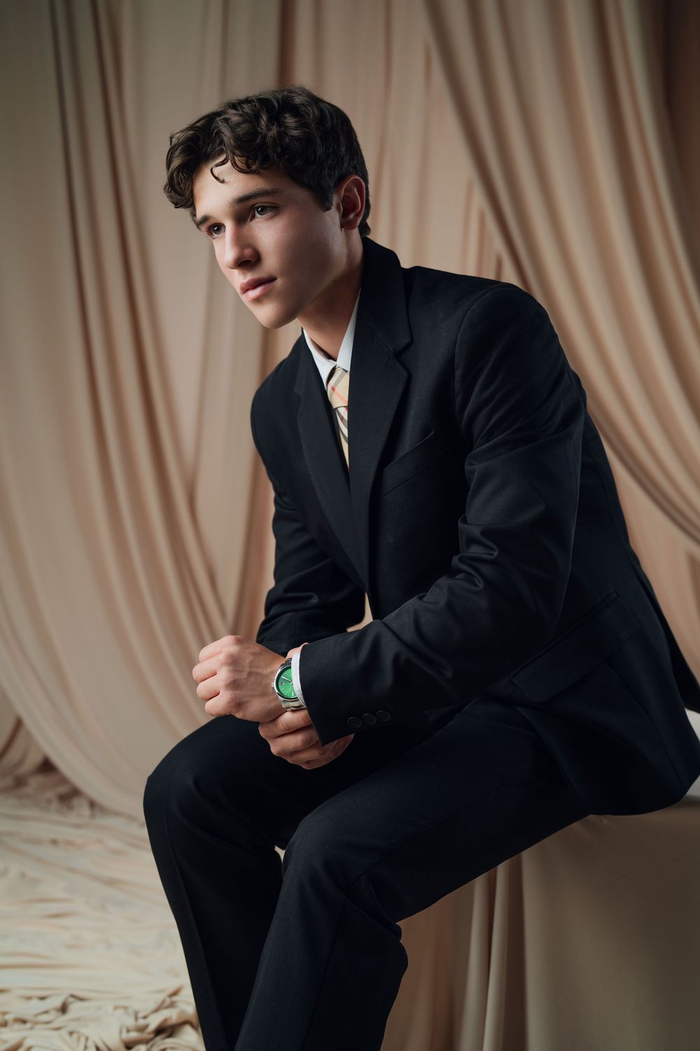 Studio portrait session with black suit against elegant draped fabric background.