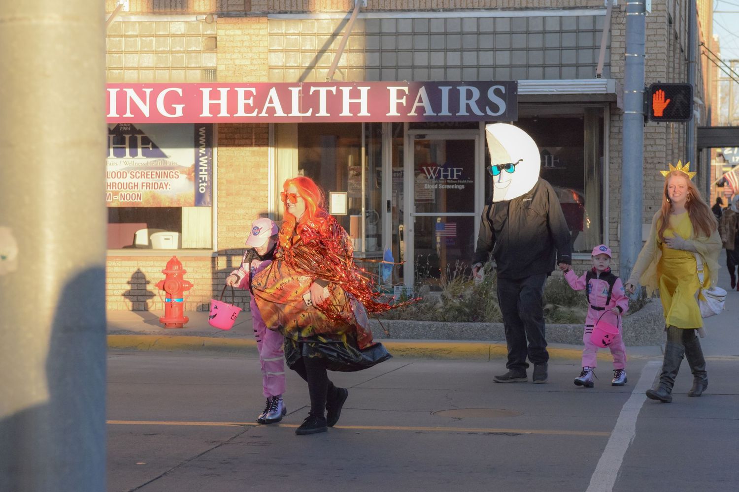 A person in a colorful chicken costume crossing the street during a community event.