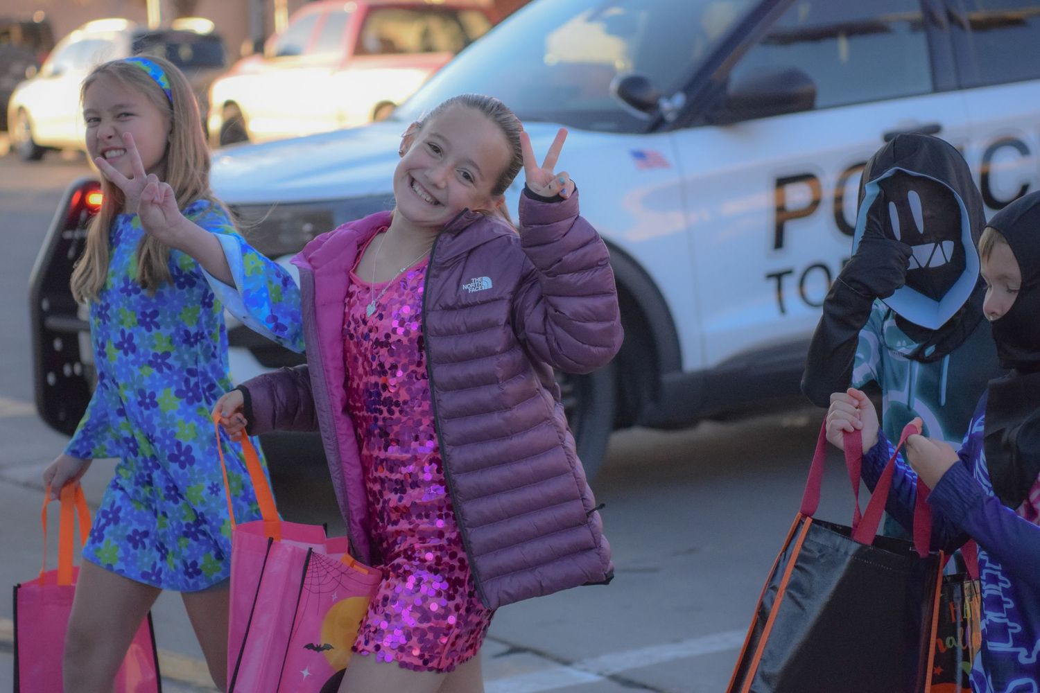 Children in colorful winter coats walk together in a line outside a storefront.