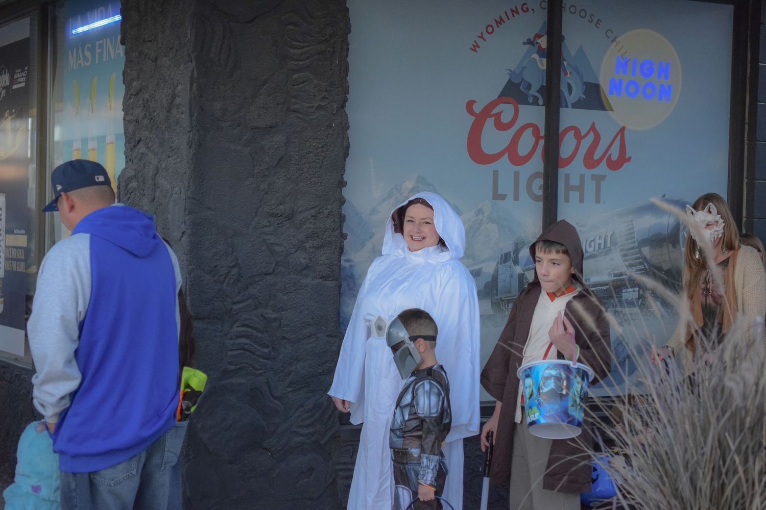 People gather outside a storefront with neon signs visible in the background.