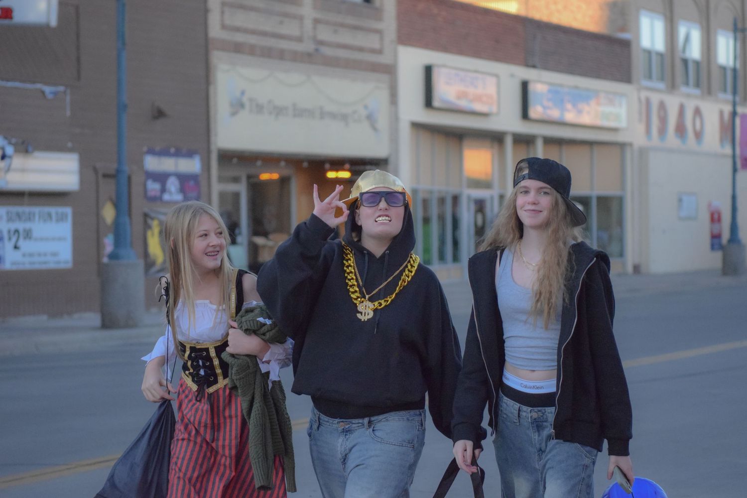 People stand in line outside a row of retail storefronts at dusk.