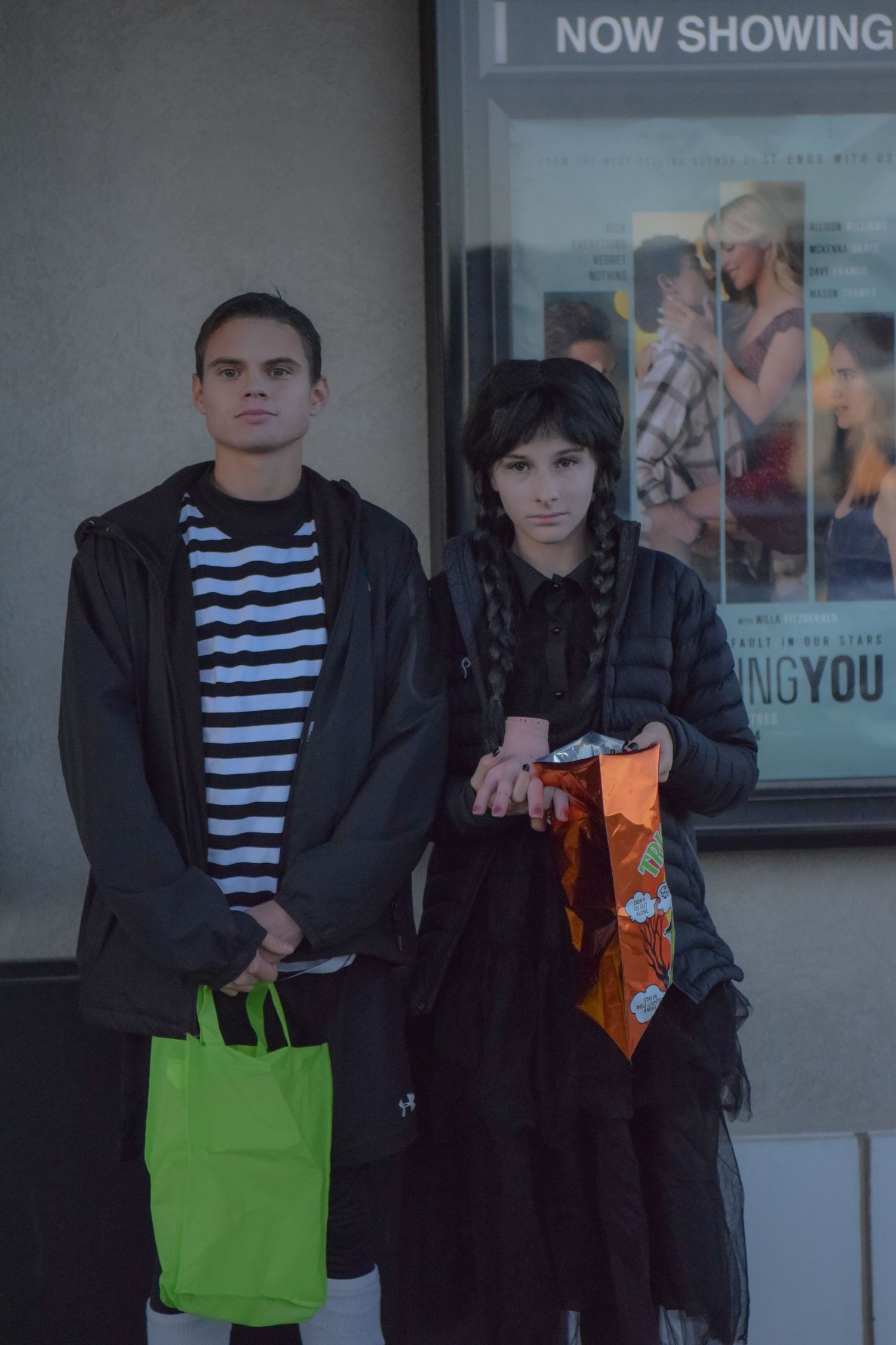 People stand outside a movie theater with trick-or-treat bags during a Halloween event.