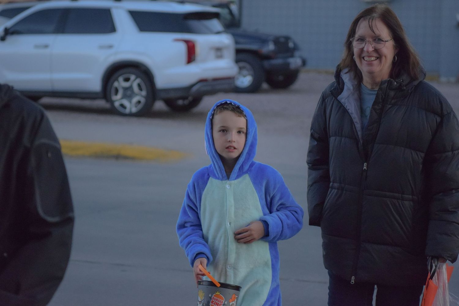 Children in winter coats walk along a street during a Halloween event.