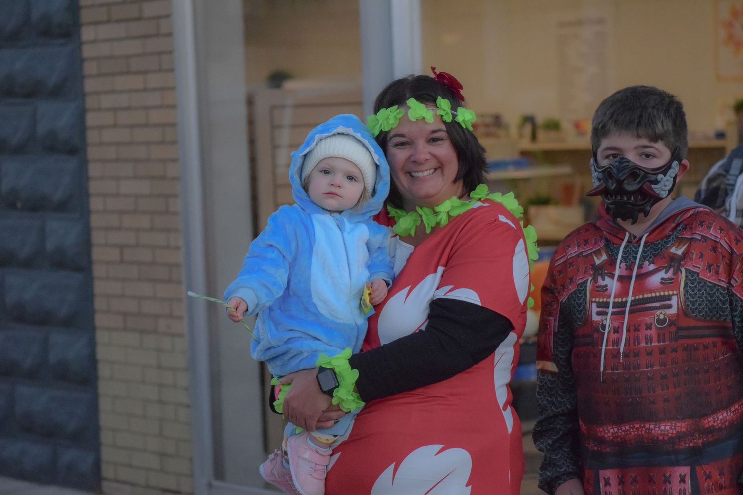 Colorful Halloween costumes are displayed as people gather outside a storefront.