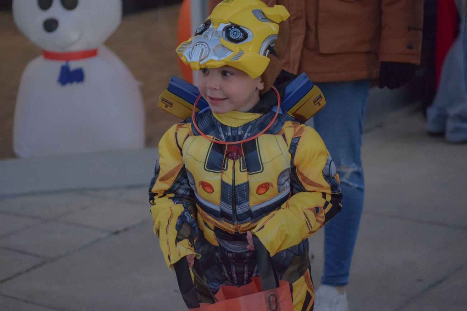 A child wearing a bright yellow costume stands among other Halloween trick-or-treaters.