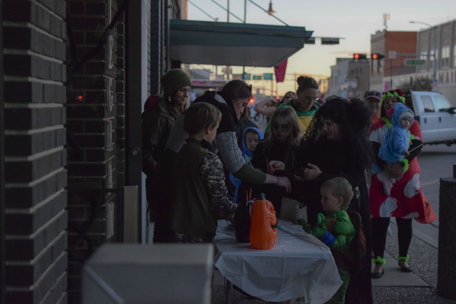 A line of people wait outside storefronts during a Halloween event.