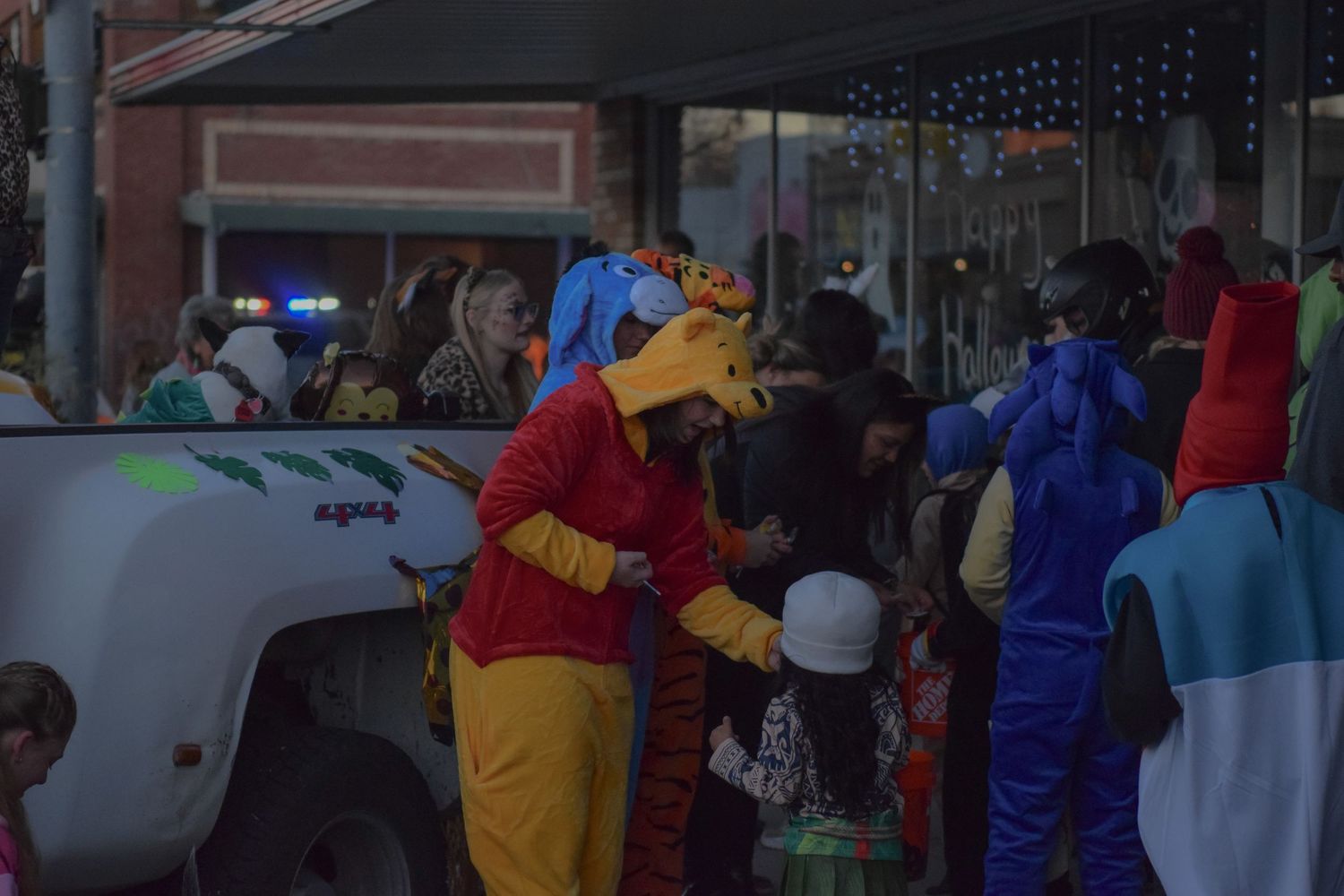A crowd of costumed trick-or-treaters gather outside businesses during Halloween.