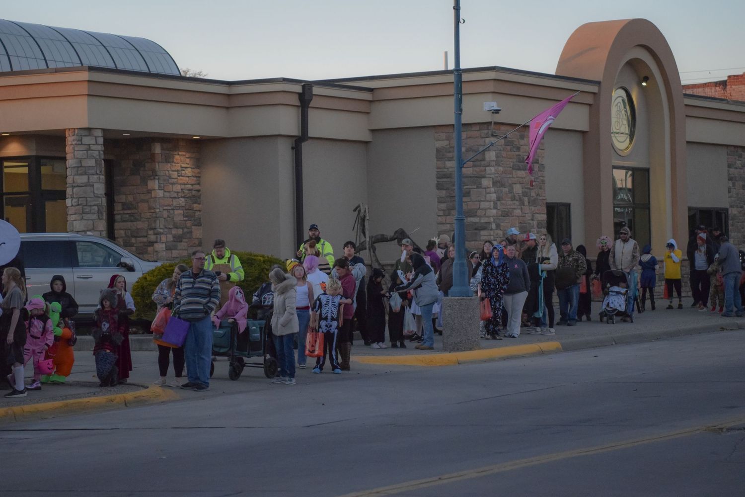 A long line of people extends along a shopping center exterior during a Halloween event.