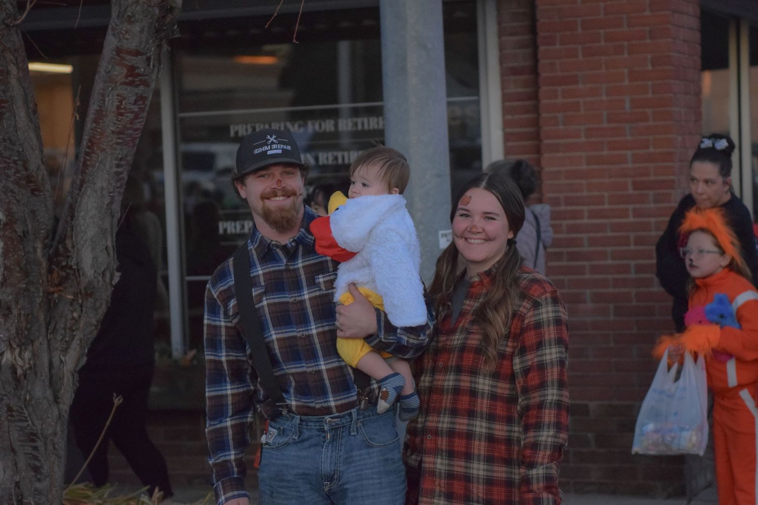 People gathered outside a brick building for a Halloween event wearing costumes and carrying candy bags.
